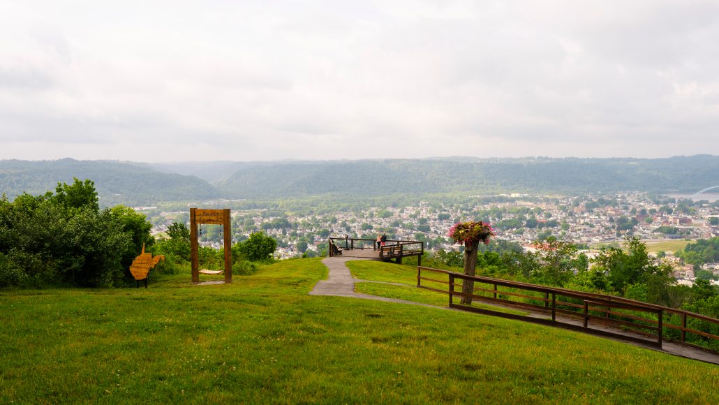 Scenic view from a hilltop overlooking a town, with a wooden frame and flower planter in the foreground.