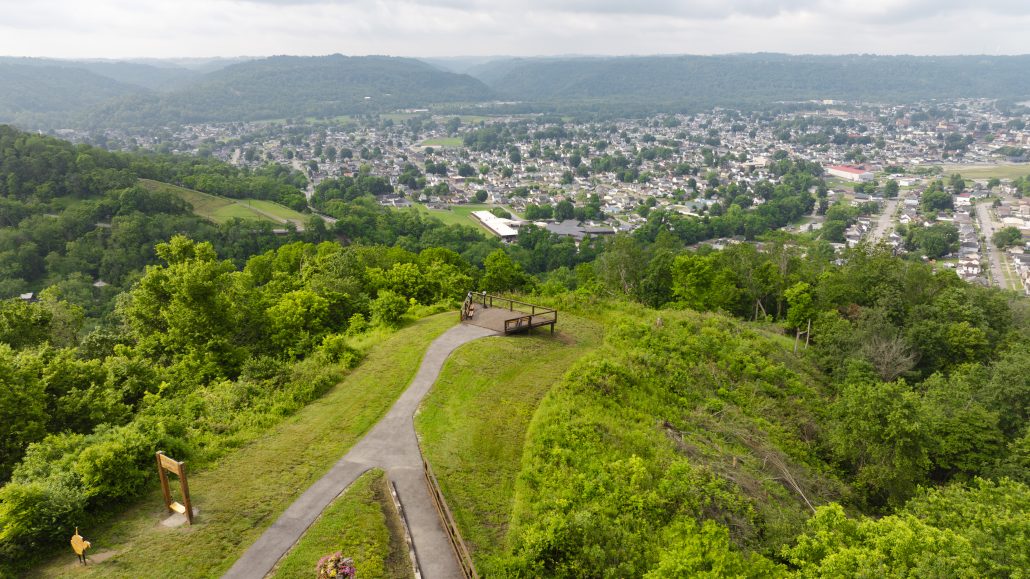 Aerial view of a green hillside overlooking a town with houses and trees, featuring a wooden observation deck.