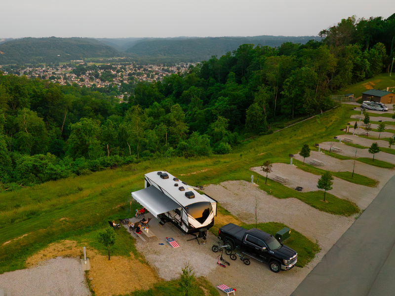 Aerial view of a camper and truck parked in a green area with a town visible in the background.