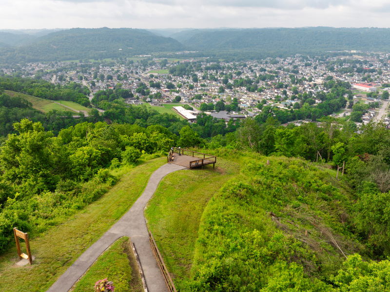 Aerial view of a green hillside overlooking a small town with buildings and roads, under a cloudy sky.